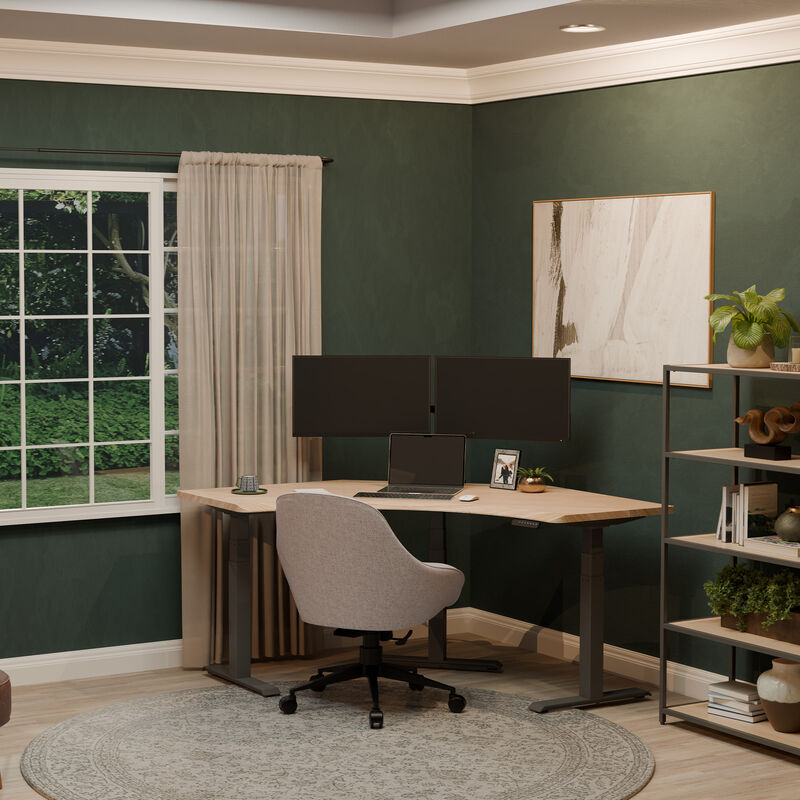 A minimalist home office featuring a light wood L-shaped standing desk with dual monitors, a laptop, and a cozy upholstered chair, set against dark green walls and a large window with garden views. image number null